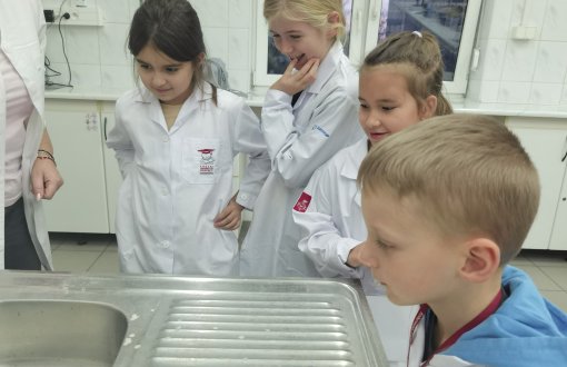 Dzieci w wfartuchcach w laboratorium mikrobiologicznym obserwują doświadczenie